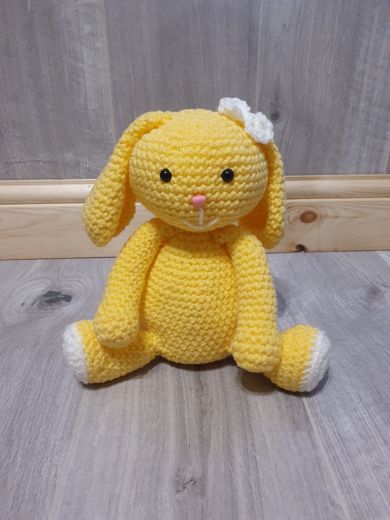 A hand-crocheted amigurumi bunny in bright yellow with a white bow