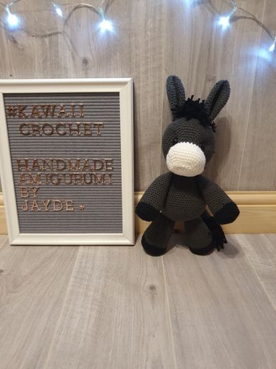 A hand-crocheted amigurumi donkey in charcoal grey with a cream muzzle