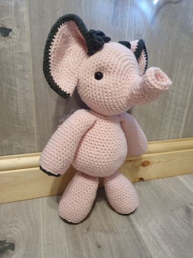 A hand-crocheted amigurumi elephant in pale pink with dark grey ears