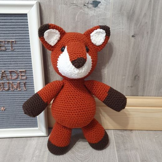A hand-crocheted amigurumi fox in orange and white, sitting up