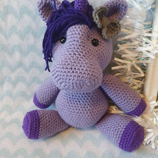 A hand-crocheted amigurumi pony in lilac with a dark purple mane