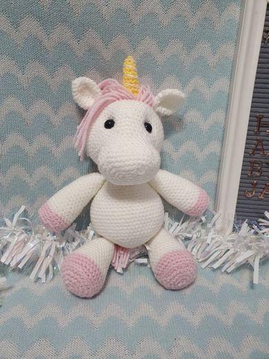 A hand-crocheted amigurumi unicorn in white and pink with a golden horn