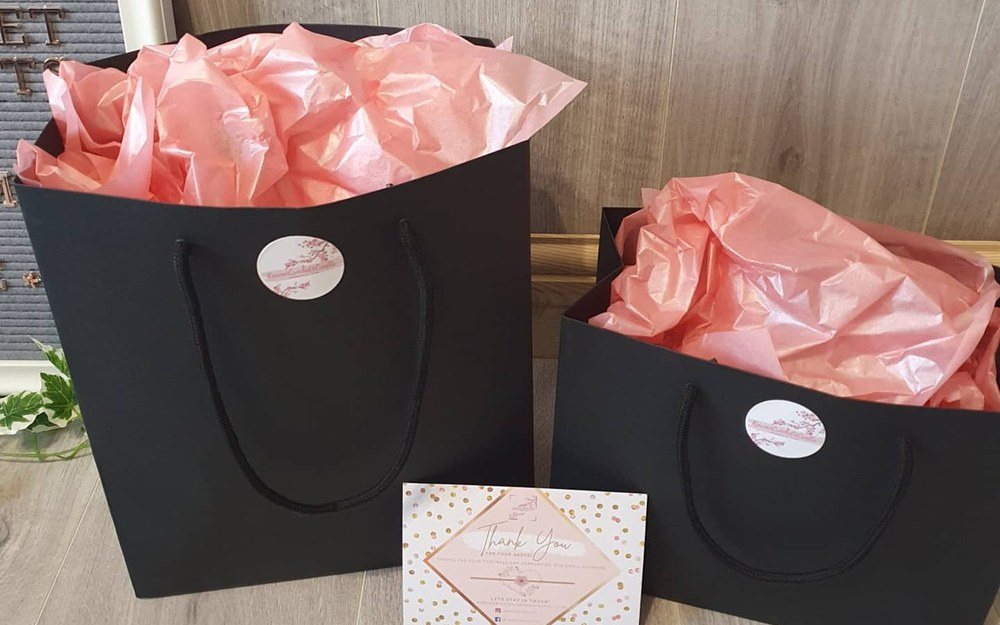Black gift bags with pink tissue paper and a thank-you card, ready to post